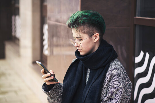 A modern girl in casual clothes uses a smartphone on a city street in autumn. Social networks, communication.