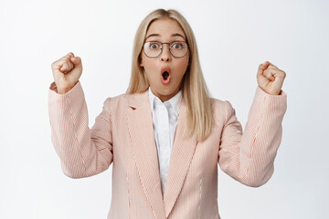 Wall Mural - Surprised saleswoman celebrating, looking amazed and cheering, chanting from awesome news, standing against white background