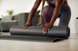 © Drazen - Close-up of African American athlete rolls up her Yoga mat in living room.