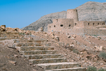 Wall Mural - Stone walls of small medieval Arabian fort under tall mountain cliffs. Fortress in Bukha, Musandam peninsula, Oman. Hot, hazy day in Arabian desert.