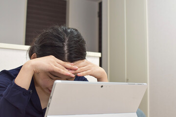 A young Asian woman gets depressed and holds her head during telework