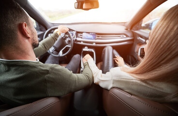 Top view of pair in love in cabin of luxury car. Man driver and his girlfriend on front passenger seat holding each other's hand tightly. Romantic moments of two lovers while riding automobile.