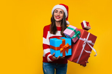 Wall Mural - Close up photo of beautiful excited smiling woman with many cool Christmas gift boxes in hands while she is having fun and posing on yellow background