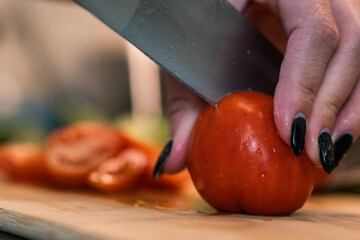 Home cooking. Slicing tomatoes with a knife on a wooden board.