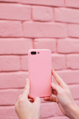hands holding a mobile phone in pink case with pink brick wall as background