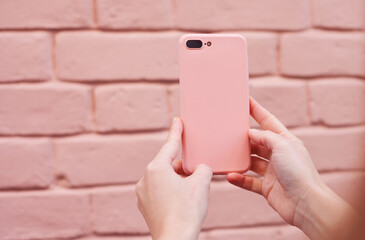 hands holding a mobile phone in pink case with pink brick wall as background. barbiecore style aesth