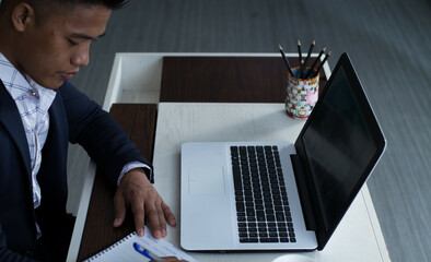 Poster - Southeast Asian businessman working on a laptop and taking notes