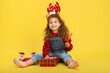 © nellas - Little girl for the Christmas holidays with a gift and a lollipop on a yellow background to copy  space