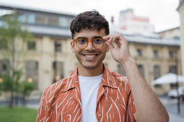 Portrait of handsome smiling Indian man wearing casual clothing, hipster eyeglasses looking at camera standing on the street 