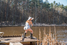 A Girl Stands On The Shore Of A Forest Lake And Catches Fish With A Fishing Rod.