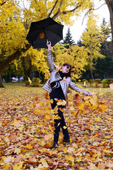 happy attractive laughing brunette in dark glasses holds an umbrella over her head, from which autumn yellow leaves fall and fly. Lady enjoys autumn nature and smiles carelessly