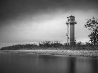 calm water and view to lighthouse under dark sky in photo of vintage style