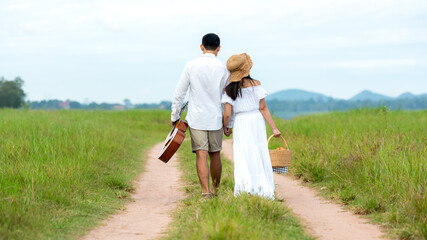 Wall Mural - Lifestyle couple picnic sunny time. Asian young couple having fun and walking relax in the meadow and field in holiday.  Romantic and In love.   Lifestyle concept