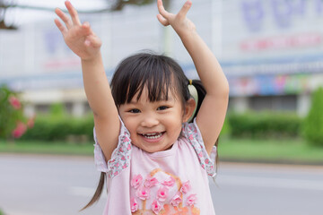 Wall Mural - Portrait​ image of​ 3-4 years old​ childhood​ child. Face of smile and laugh Asian​ girl in head shot. Happy​ kid playing​ at the park playground. In summer or spring​ season.