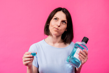 Wall Mural - Beautiful girl uses mouthwash on the pink background