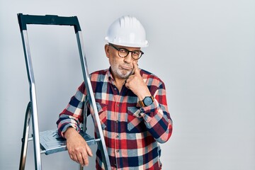 Canvas Print - Handsome mature handyman close to construction stairs wearing hardhat pointing to the eye watching you gesture, suspicious expression