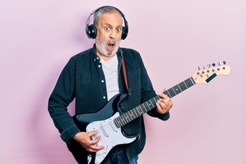 Sticker - Handsome senior man with beard playing electric guitar in shock face, looking skeptical and sarcastic, surprised with open mouth