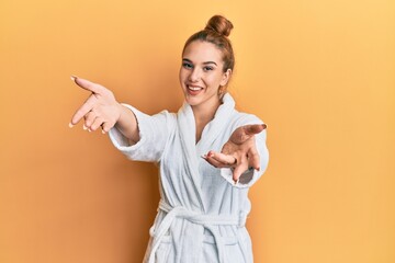 Canvas Print - Young blonde woman wearing bathrobe looking at the camera smiling with open arms for hug. cheerful expression embracing happiness.