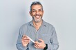Handsome middle age man with grey hair holding glucometer device smiling and laughing hard out loud because funny crazy joke.
