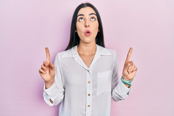 Canvas Print - Beautiful woman with blue eyes wearing casual white shirt amazed and surprised looking up and pointing with fingers and raised arms.