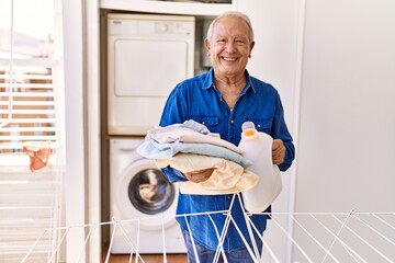 Wall Mural - Senior caucasian man holding detergent and folded clothes standing by washing machine at the terrace.