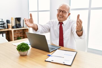 Sticker - Senior man working at the office using computer laptop looking at the camera smiling with open arms for hug. cheerful expression embracing happiness.