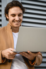Selective focus of joyful businessman in coat using laptop near building outdoors 