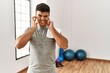 © Krakenimages.com - Young hispanic man wearing sportswear and towel at the gym covering ears with fingers with annoyed expression for the noise of loud music. deaf concept.