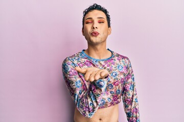 Handsome man wearing make up wearing fashion clothes looking at the camera blowing a kiss with hand on air being lovely and sexy. love expression.