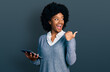 Young african american woman using touchpad device pointing thumb up to the side smiling happy with open mouth