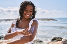 Young African American Girl Smiling Happy Using Sunscreen Lotion At The Beach.