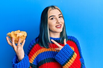 Wall Mural - Young modern girl holding potato chips smiling happy pointing with hand and finger