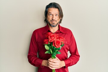 Canvas Print - Middle age handsome man holding bouquet of red roses puffing cheeks with funny face. mouth inflated with air, catching air.