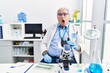 © Krakenimages.com - Senior caucasian man working at scientist laboratory in shock face, looking skeptical and sarcastic, surprised with open mouth