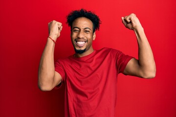 Young african american man with beard wearing casual red t shirt celebrating surprised and amazed for success with arms raised and open eyes. winner concept.