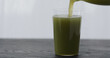 pour green matcha drink in tumbler glass on black oak table with copy space