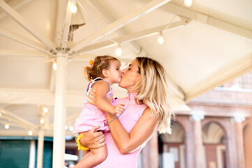 happy loving family - beautiful blond mother hugging and kissing her sweet daughter on street in the