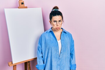 Poster - Young hispanic woman standing by painter easel stand depressed and worry for distress, crying angry and afraid. sad expression.