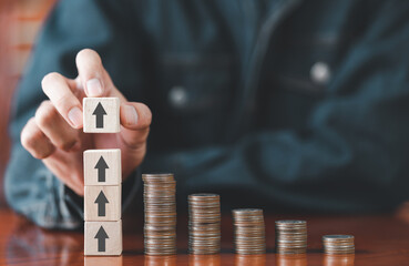 Businessman putting wooden cube box arrow with stack coins on desk. Saving money, bank deposits, interest collection and tax concept. Upward trend in business growth, financial management