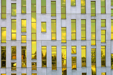 Fragment of office building facade made of yellow toned glass and concrete constructions. Frontal view. Reflection of the sky and cityscape in the mirrored windows. Katowice, Silesia, Poland.