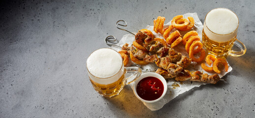 Top view of two glasses of foamy beer served with onion crisps and meat, copy space