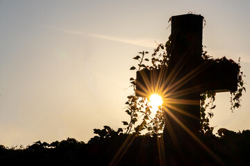 Glowing cross silhouette with sunbeams sunset sunlight and clear evening sky shows christianity spirituality of church and forgiveness at grave and death for catholic resurrection metaphors on easter