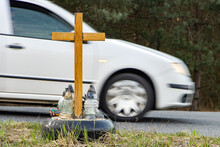 A Roadside Memorial Cross With A Candles Commemorating The Tragic Death, On A Background Ride Blurred Car.