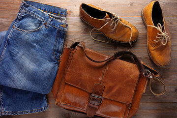 Wall Mural - Denim jeans and old boots with leather bag at wood table. Travel concept as retro clothes