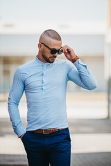 Canvas Print - Cool handsome Caucasian man wearing a light blue shirt and sunglasses posing outdoor