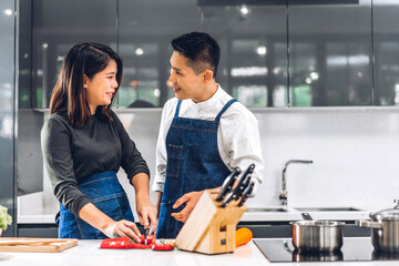 Wall Mural - Young asian family couple having fun cooking together with fresh vegetable healthy food clean on table.Happy couple prepare the food yummy eating lunch in kitchen