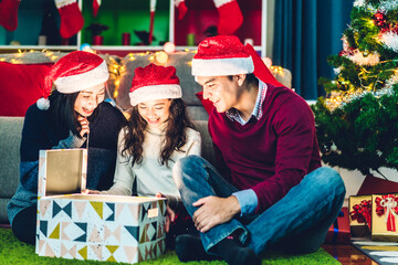 Portrait of happy family father and mother with daughter in santa hats having fun opening magic christmas gift box and enjoying spending time together in christmas time at home