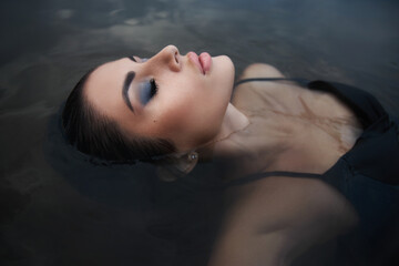 beauty brunette woman in a black dress poses in a sea lake against a blue sky background. long hair 