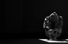Light And Shadow On Surface Of Hopeless Man In Hoody Sitting Alone With Hugging His Knees On The Floor In Empty Dark Room In Black And White Style