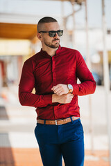 Wall Mural - Cool handsome Caucasian man wearing an elegant red shirt and sunglasses posing outdoor